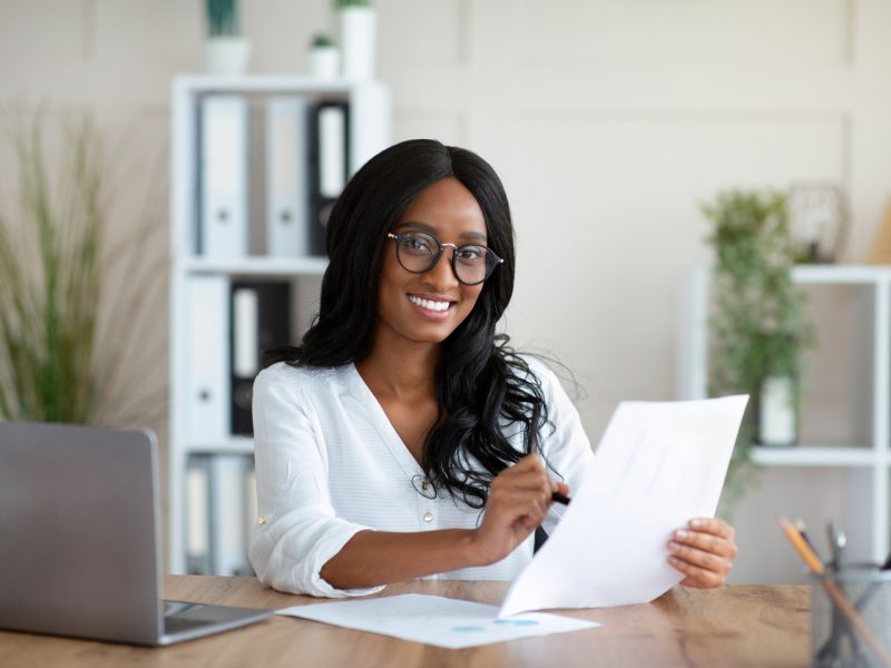 Beautuful black business lady working with documents at desk in office. African American female entrepreneur looking frough important contract or agreement at her workplace